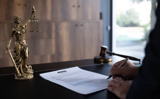 Person signing a contract beside a Lady Justice statue and a gavel