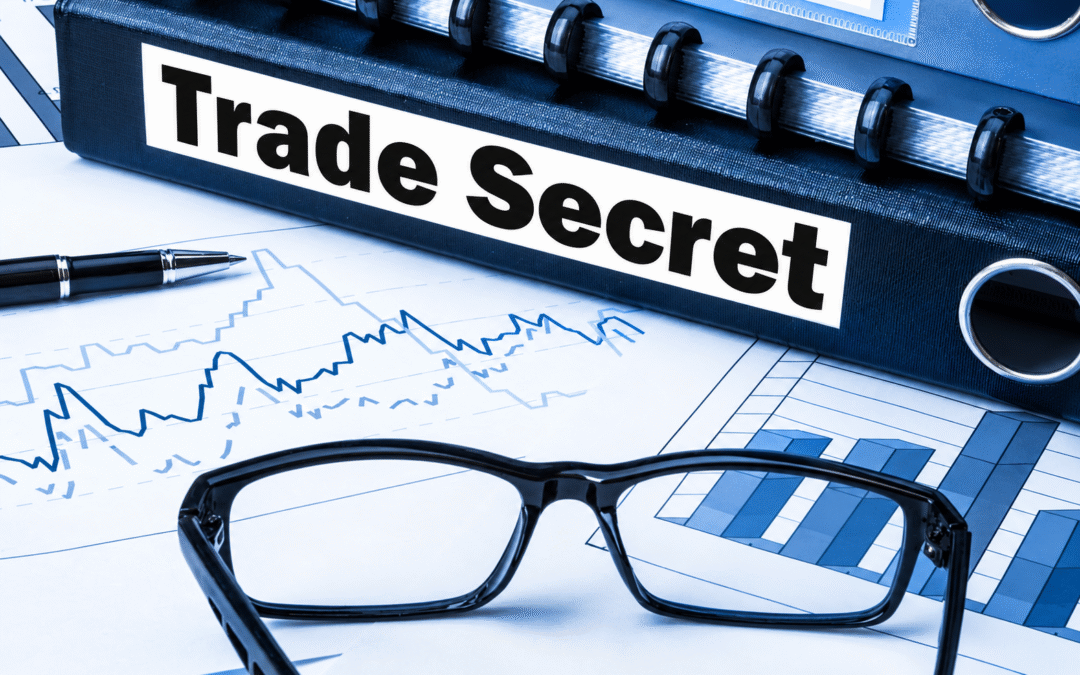 Trade secret binder on a desk with financial charts, a pen, and eyeglasses