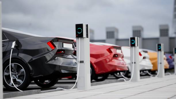 Row of electric vehicles, including black, red, and white cars, connected to charging stations in a modern outdoor charging facility