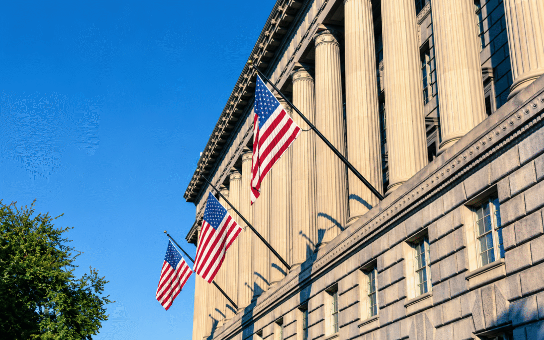 Neoclassical building with tall stone columns and American flags displayed against a clear blue sky