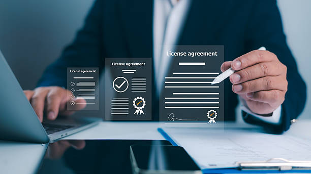 Business professional reviewing a digital license agreement with approval and certification icons, alongside a laptop and documents on a desk