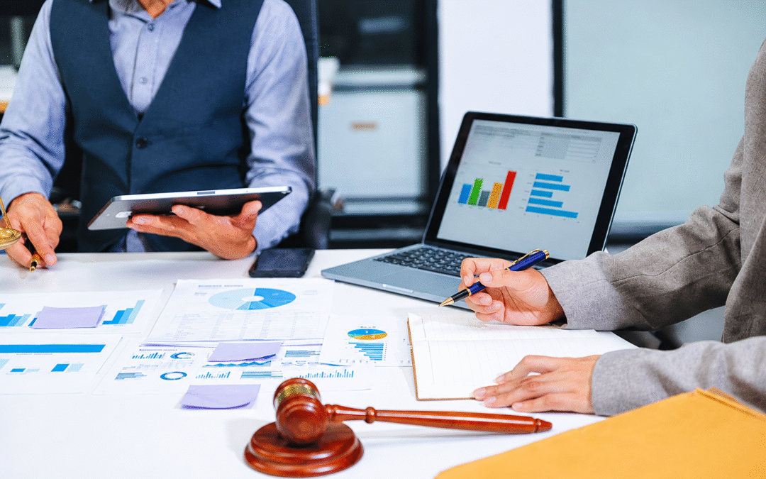 Business professionals reviewing charts and documents during a meeting with a laptop, tablet, and legal gavel on the table